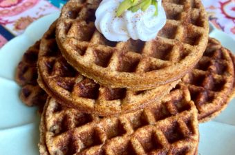 Plated Gluten-free Pumpkin Waffles topped with whipped cream pumpkin spice and green pistachios
