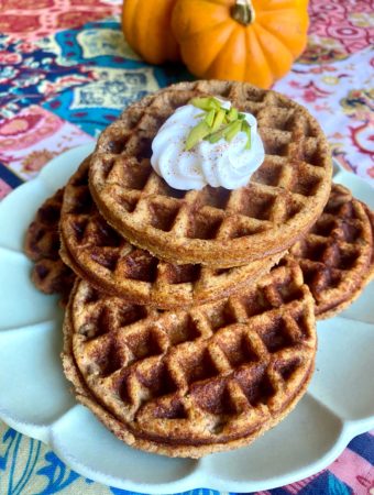 Plated Gluten-free Pumpkin Waffles topped with whipped cream pumpkin spice and green pistachios