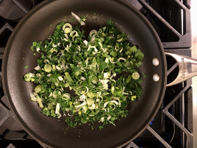 Cooking fresh herbs and onions in a pan