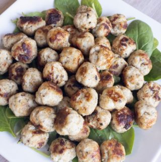 Lean ground turkey meatballs served on a platter of baby spinach leaves