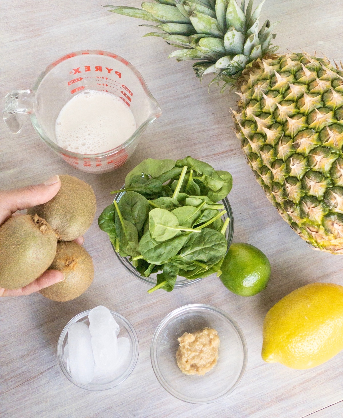Ingredients for green goddess smoothie: kiwi, ice, ginger, spinach, milk, lemon, lime and pineapple.